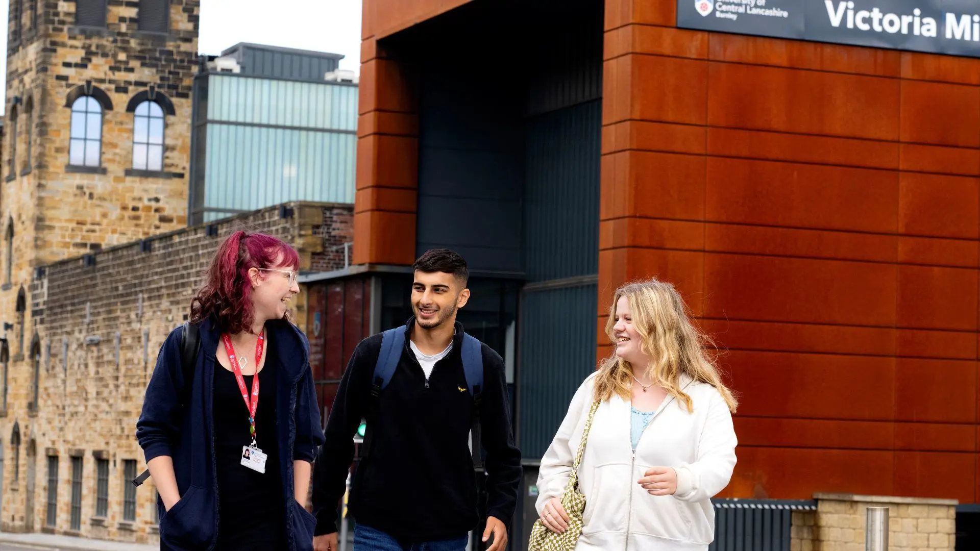 Three students walk and chat outside Victoria Mill.