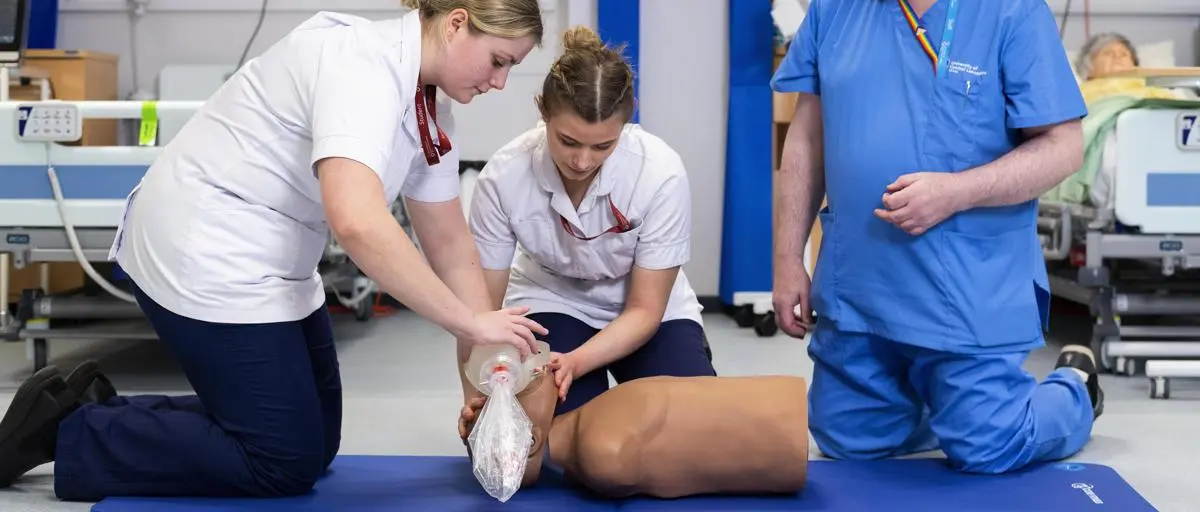 A pair of student nurses, along with a tutor, practice CPR on a medical dummy.