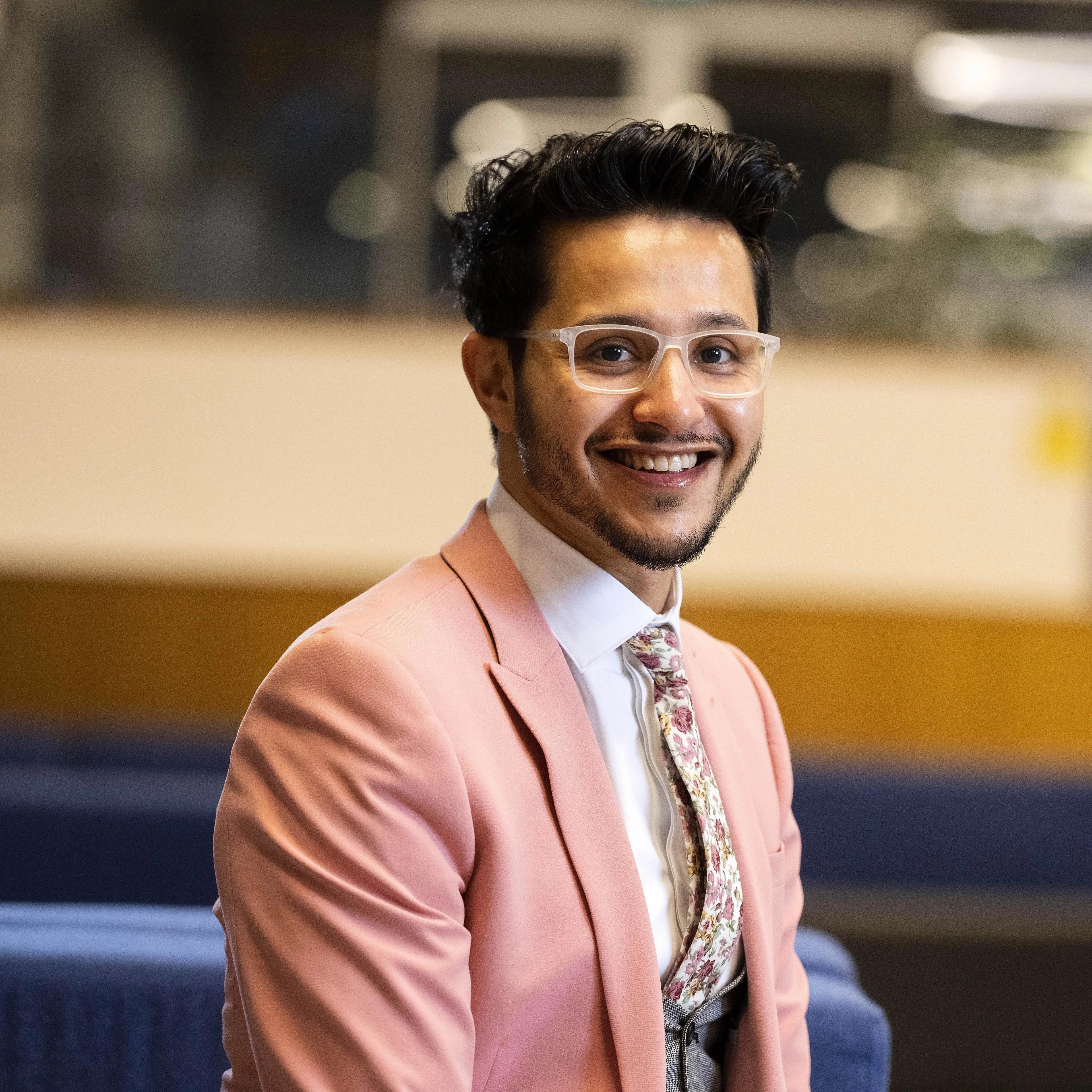 Emad in a pink suit and glasses smiling