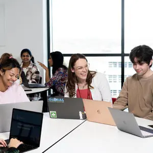 Postgraduate research students studying with laptops in bright classroom