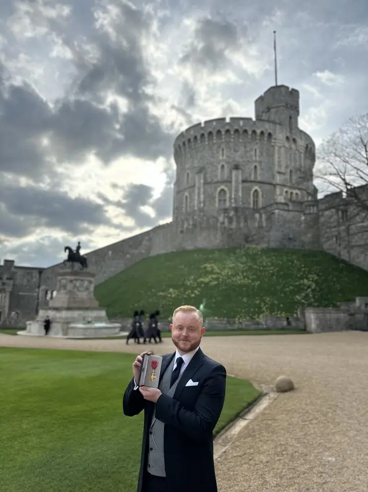 Travis Frain holding his OBE medal outside Windsor Castle