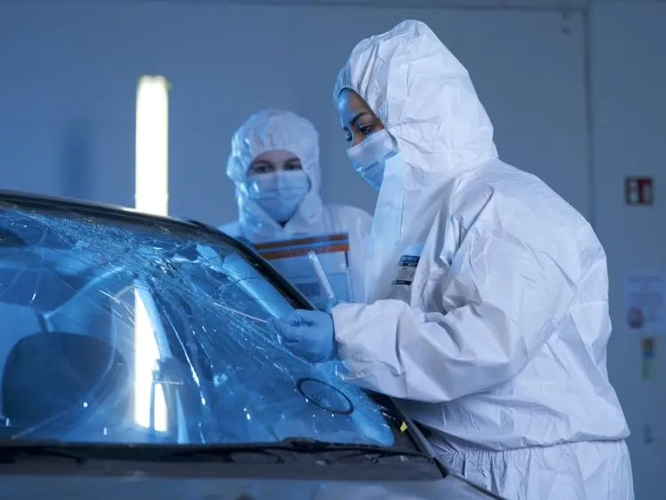 Forensics person dressed in coverall swiping front of a broken car window